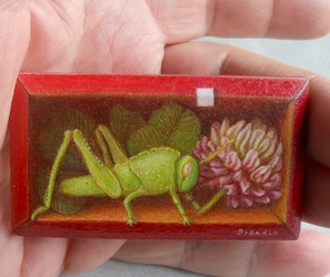 Miniature en trompe l oeil representant une sauterelle verte et un trefle dans une petite boite